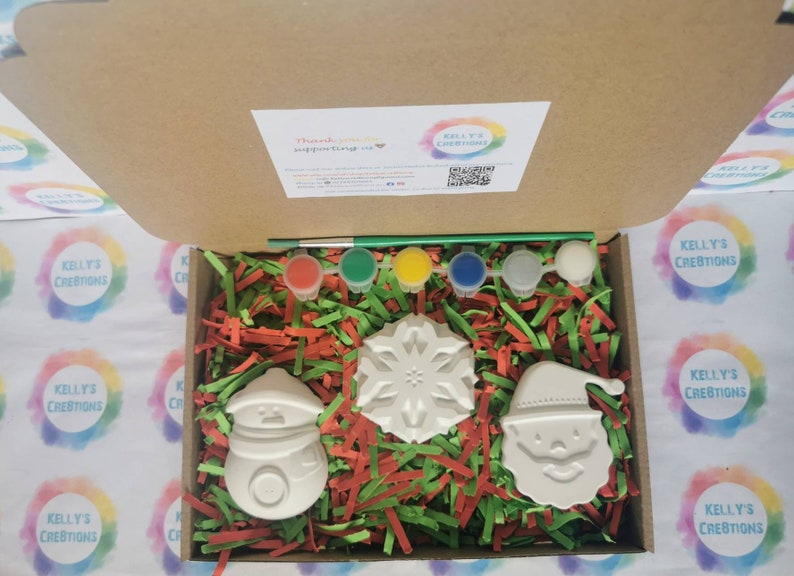 Pu&ograve; includere: Un kit di ceramica fai-da-te a tema natalizio con un pupazzo di neve, Babbo Natale e un fiocco di neve. Il kit include cinque barattoli di vernice, un pennello e carta triturata verde e rossa.