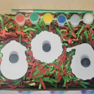 Pu&ograve; includere: Un set di tre ornamenti in ceramica bianca a forma di pupazzo di neve, una ghirlanda e Babbo Natale. Gli ornamenti hanno un foro al centro e sono circondati da carta triturata rossa e verde. Il set include cinque piccoli flaconi di vernice in rosso, verde, giallo, blu e bianco.