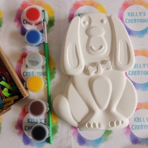 May include: White ceramic dog figurine with a bone on its collar. The figurine is ready to be painted with six small pots of paint in red, blue, gray, yellow, brown, and black.