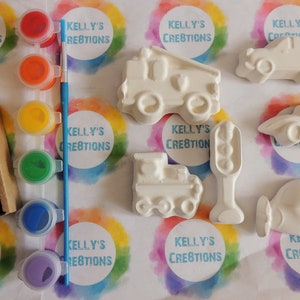 May include: A set of six white ceramic figurines of different vehicles, including a fire truck, a train, a car, a plane, a truck, and a traffic light. The figurines are ready to be painted with the included set of five paint pots in red, orange, yellow, green, and purple.