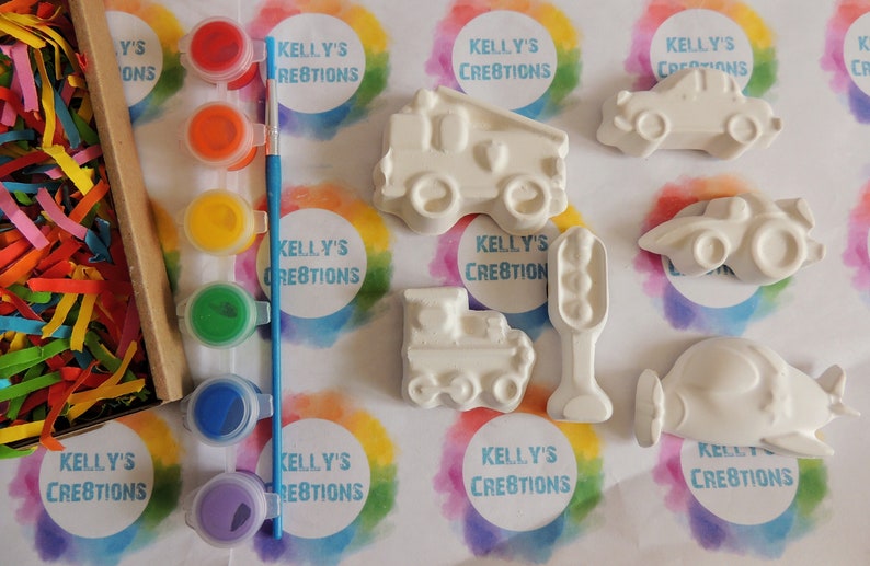 May include: A set of six white ceramic figurines of different vehicles, including a fire truck, a train, a car, a plane, a truck, and a traffic light. The figurines are ready to be painted with the included set of five paint pots in red, orange, yellow, green, and purple.