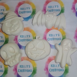 May include: Set of six white ceramic Halloween-themed ornaments. The ornaments include a pumpkin, a ghost, a bat, a skull, and two more pumpkins. Each ornament has a blank surface for painting or decorating.