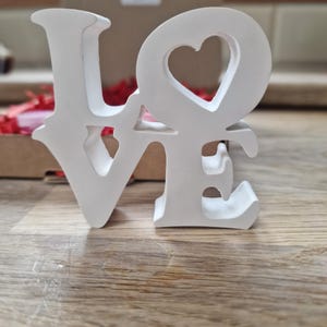 May include: White wooden letters spelling "LOVE" with a heart cut out of the "O".