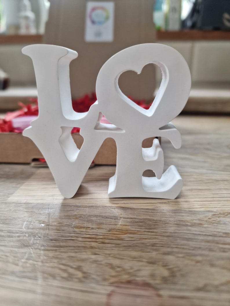 May include: White wooden letters spelling "LOVE" with a heart cut out of the "O".