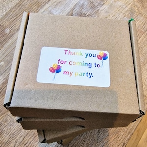 May include: A brown cardboard box with a white sticker that says "Thank you for coming to my party." The sticker has a colourful balloon graphic.