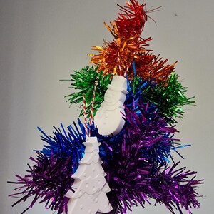 May include: White ceramic Christmas ornaments in the shape of a snowman and a Christmas tree hanging from a rainbow tinsel tree.