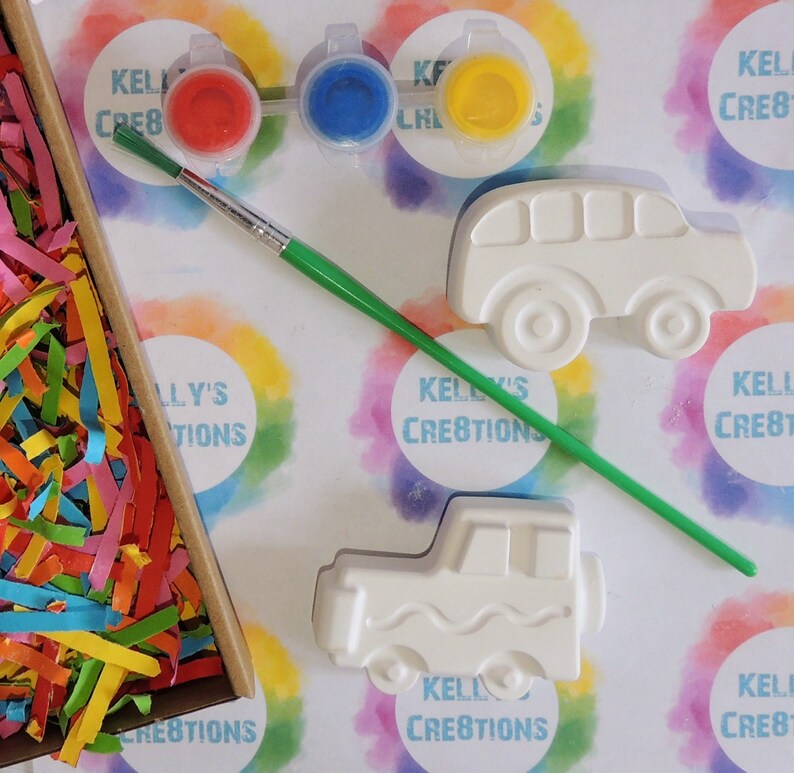 Puede incluir: Un kit de manualidades con figuras de cer&aacute;mica con forma de autob&uacute;s y cami&oacute;n, botes de pintura roja, azul y amarilla y un pincel. El kit incluye papel triturado de colores y el texto "Kelly's Creations".