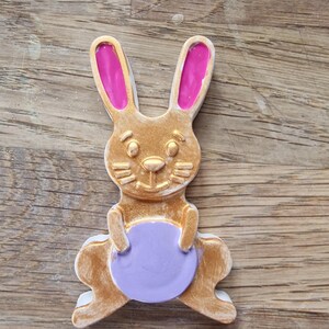 May include: A gold bunny rabbit figurine with pink ears holding a purple egg.