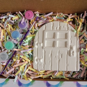 May include: A white ceramic door with a window and a keyhole, surrounded by colorful shredded paper and paint pots.