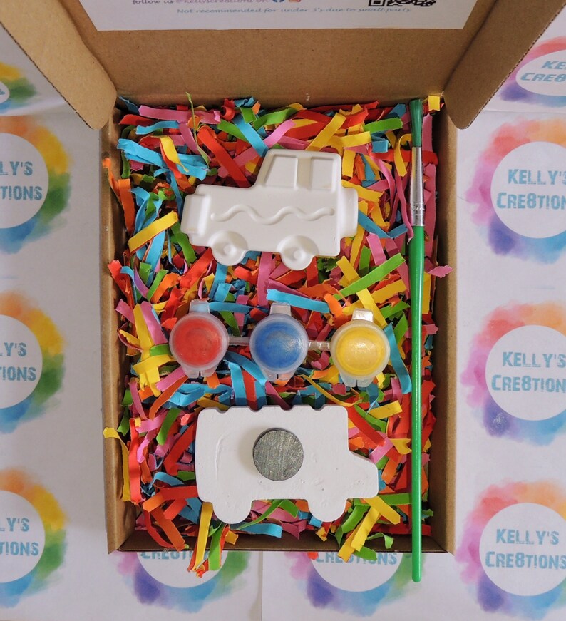 Puede incluir: Un kit de manualidades en una caja de cart&oacute;n, con una pieza de cer&aacute;mica blanca en forma de cami&oacute;n, botes de pintura roja, azul y amarilla, y un pincel verde. La caja est&aacute; llena de papel triturado de colores. Tambi&eacute;n se incluye una segunda pieza en forma de cami&oacute;n con un im&aacute;n.