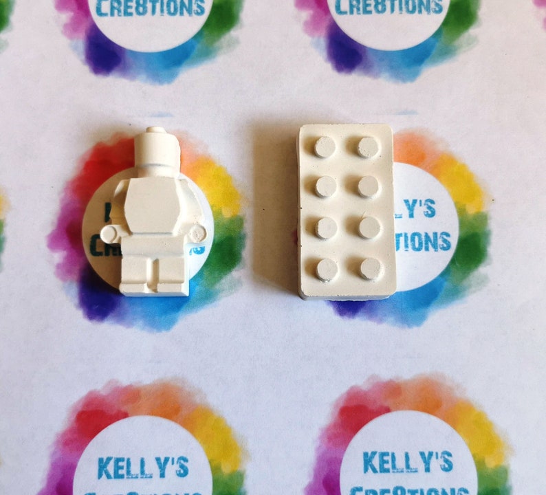 Puede incluir: Dos figuritas de hormig&oacute;n blanco en miniatura de un personaje Lego y un ladrillo Lego. Las figuritas est&aacute;n sobre una superficie blanca con c&iacute;rculos de colores.