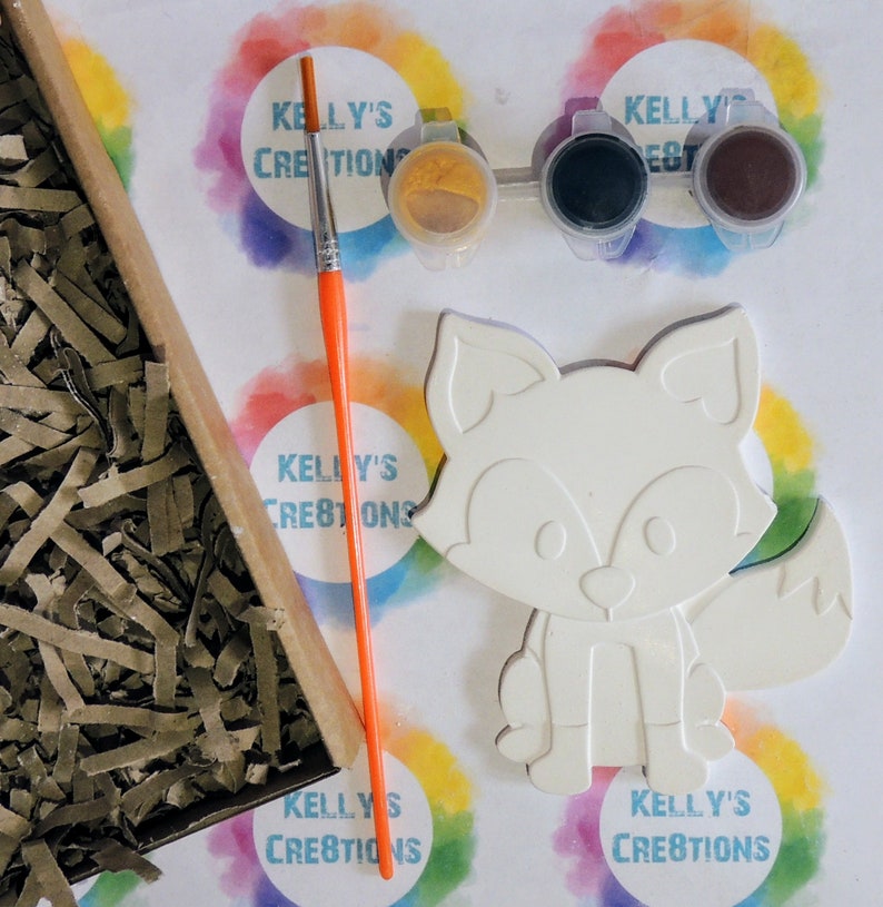 May include: A white ceramic fox figurine with paint-by-numbers outlines. The kit includes three small paint pots with lids, a paintbrush, and a sheet of paper with the Kelly's Creations logo.