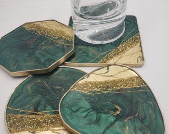 May include: Set of four green and gold coasters with a marbled design. The coasters have a gold rim and are made of resin.