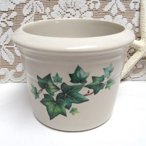 May include: A white ceramic planter with a green ivy design. The planter is round and has a wide rim.