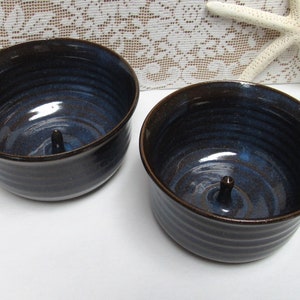 May include: Two dark brown ceramic bowls with a blue glaze. Each bowl has a small knob in the center of the bottom.