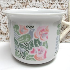May include: White ceramic planter with a floral and bird design. The design features pink, green, and blue colors.