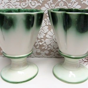 May include: Two white ceramic vases with green glaze. The vases have a flared top and a pedestal base.