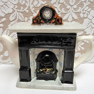 May include: A white ceramic teapot shaped like a fireplace with a black mantel and a clock on top. The fireplace has a black stove with a fire inside and a blue and white tiled backsplash.