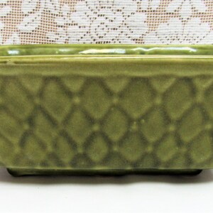 May include: A square green ceramic planter with a diamond pattern. The planter has a slightly flared rim and a flat base.