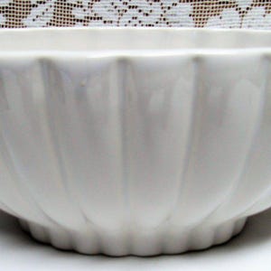 May include: A white ceramic bowl with a scalloped design. The bowl has a wide, open shape and a textured, ribbed exterior. The bowl is likely used for serving or display purposes.