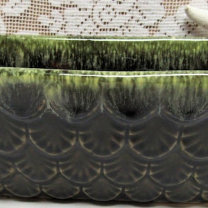 May include: A rectangular, dark green ceramic planter with a scalloped pattern on the sides. The planter has a glossy finish with a darker green base and lighter green highlights near the rim. The planter is likely for indoor or outdoor use.
