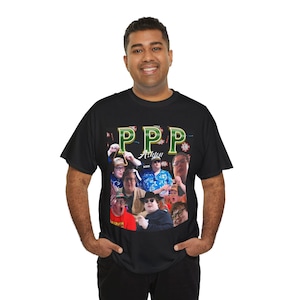 Puede incluir: Camiseta negra con un collage de imágenes y el texto "PPP Action". El diseño incluye múltiples caras y el texto "Ashton" en una combinación de colores verde y dorado. La camiseta la lleva una persona.