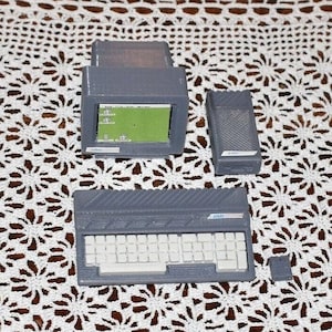 Puede incluir: Un ordenador gris y blanco con un monitor pequeño, un teclado y una caja separada. El ordenador está sobre un mantel de ganchillo blanco.