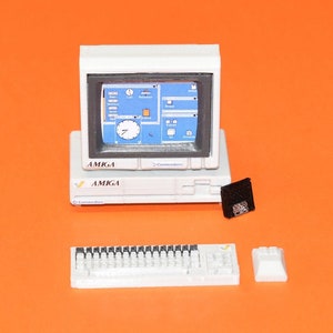 Può includere: Un computer Amiga bianco con un monitor, una tastiera e un'unità floppy disk. Il monitor mostra uno schermo blu con un orologio e altre icone.