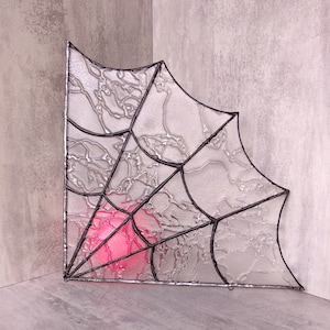 Può includere: Un vetro colorato a forma di ragnatela con una luce rosa che lo attraversa.