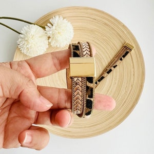 May include: A gold and brown multi-layered bracelet with a leopard print design and a gold clasp.