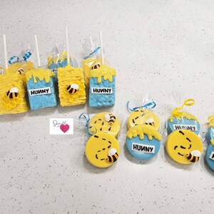 May include: A collection of decorated treats, including blue and yellow Rice Krispie treats and cookies. The treats are decorated with honey and bee designs, and the word "HUNNY". Some treats are on sticks and wrapped in clear cellophane.