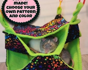May include: A multi-level fabric hammock for small pets featuring a black exterior with a colorful star pattern and a bright lime green interior. A gray and white rat is sleeping inside. Text reads: CUSTOM MADE! CHOOSE YOUR OWN PATTERN AND COLOR.