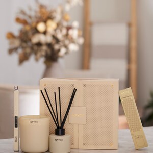 May include: A gift set of home fragrance products from the brand Nayce. The set includes a candle, a diffuser, and a candle lighter. The products are packaged in a beige box with a geometric pattern.
