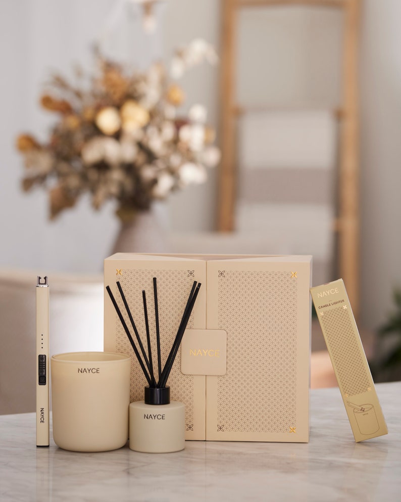 May include: A gift set of home fragrance products from the brand Nayce. The set includes a candle, a diffuser, and a candle lighter. The products are packaged in a beige box with a geometric pattern.