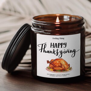May include: A lit soy wax candle in a brown glass jar with a black lid. The label reads "Happy Thanksgiving" with a roasted turkey illustration. The candle is eco-friendly and made in the USA.