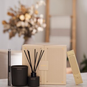 May include: A set of three black and gold scented home fragrance products. The set includes a candle, a diffuser, and a candle lighter. The products are packaged in a box with a geometric pattern.