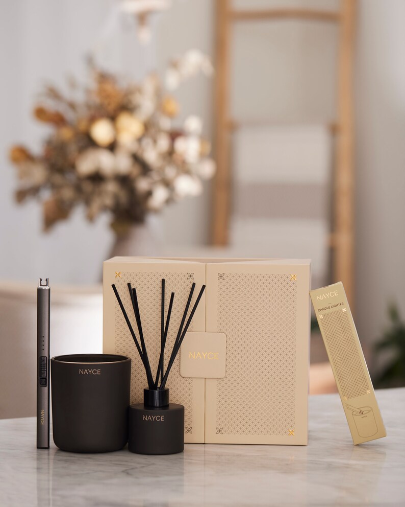 May include: A set of three black and gold scented home fragrance products. The set includes a candle, a diffuser, and a candle lighter. The products are packaged in a box with a geometric pattern.