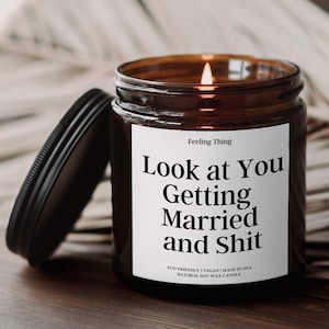 May include: A brown glass candle jar with a white label that reads "Feeling Thing Look at You Getting Married and Shit" and "ECO-FRIENDLY | VEGAN | MADE IN USA NATURAL SOY WAX CANDLE".