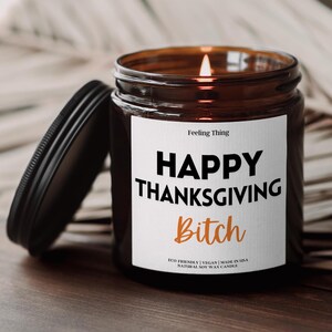 May include: A lit soy wax candle in a brown glass jar with a black lid. The label reads "HAPPY THANKSGIVING Bitch" in black and orange text. The candle is eco-friendly and vegan.