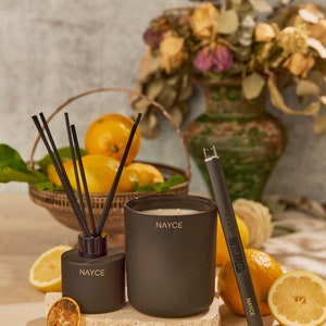 May include: A black candle, diffuser, and lighter with the word "NAYCE" printed on each. The candle and diffuser are on a stone surface with lemons and dried lemon slices around them.