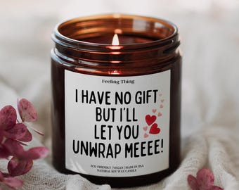 May include: A brown glass candle with a white label that reads "I have no gift but I'll let you unwrap meeee!" with pink hearts. The candle is eco-friendly, vegan, and made in the USA. It is a natural soy wax candle.