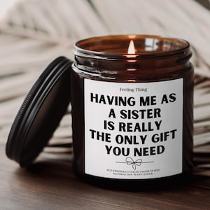 May include: A brown glass candle with a white label that reads "Having me as a sister is really the only gift you need." The label also includes the text "Feeling Thing", "Eco-friendly | Vegan | Made in USA", and "Natural Soy Wax Candle".