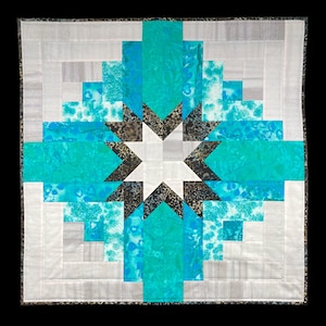 May include: A white, teal, and black quilt with a starburst pattern in the center. The quilt is made of fabric squares sewn together in a geometric design.