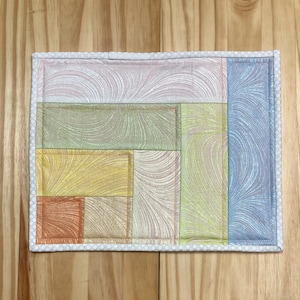 May include: A patchwork quilt coaster with a white border and a variety of colors and patterns, including pink, green, yellow, and blue.
