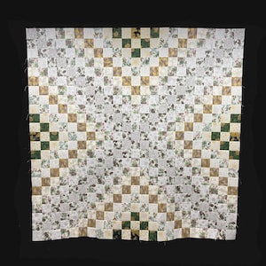 May include: A quilt with a checkered pattern in shades of white, gold, and green. The quilt is made up of small squares, each with a different floral print. The quilt is displayed on a black background.