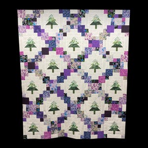 May include: A white quilt with a repeating pattern of green trees and purple and blue floral fabric squares.