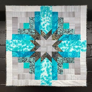 May include: A quilt with a star design in the center. The quilt is made of blue, gray, and black fabric. The star is made of gray fabric and is surrounded by blue and black fabric.