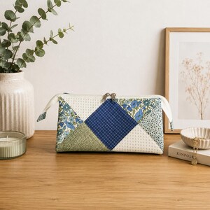 Può includere: Un beauty case patchwork rettangolare con chiusura a zip. La borsa presenta un design geometrico con tessuto a fantasia floreale blu, verde e bianco. Il beauty case ha una cerniera e tiranti color crema.