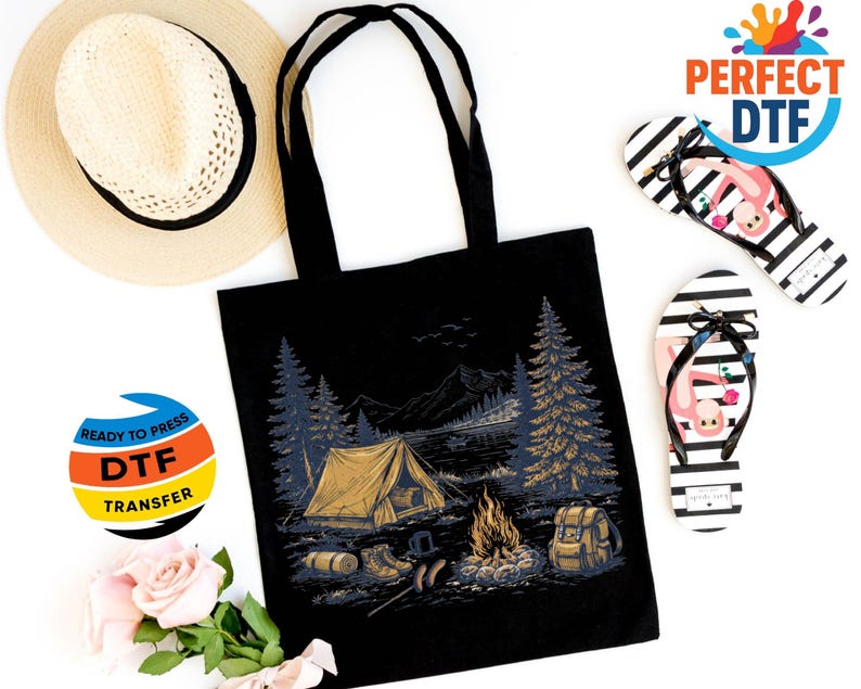 May include: Black tote bag with a camping scene graphic, a straw hat, and black and white striped flip-flops with flamingo designs. The tote bag features a tent, campfire, and forest illustration. A DTF transfer sticker is also visible.