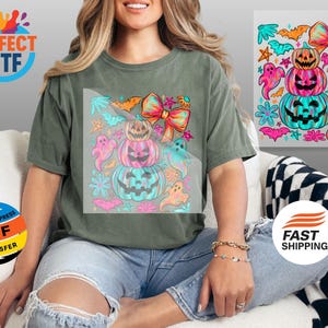 May include: Olive green t-shirt featuring a colorful Halloween design. The graphic includes stacked jack-o'-lanterns, ghosts, bows, and bats in shades of pink, teal, and orange. The shirt has the text "PERFECT DTF" and "READY TO PRESS DTF TRANSFER".